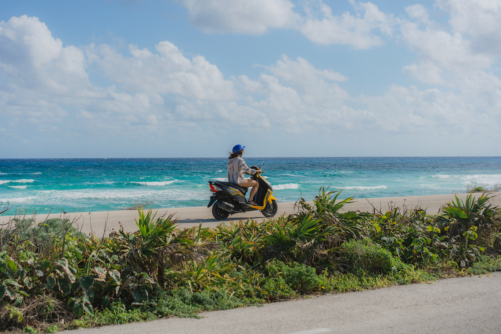 Woman driving scooter past ocean